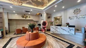 A hotel reception area with a marble reception desk, a central seating area, and a decorative ceiling.