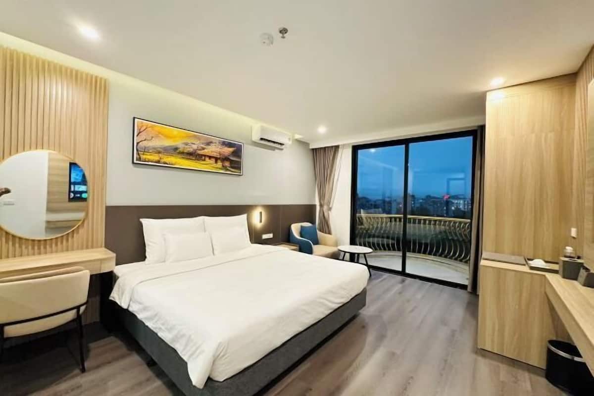 Ein modernes Hotelzimmer mit einem großen Bett, einem Schreibtisch, einem Stuhl, einem kleinen Tisch und einem Balkon mit Blick auf die Stadt.