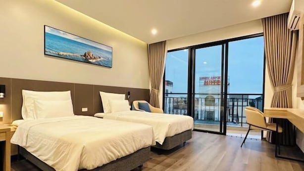 A hotel room with two beds, a desk, a chair, a large window with a view of the airport, and a painting on the wall.