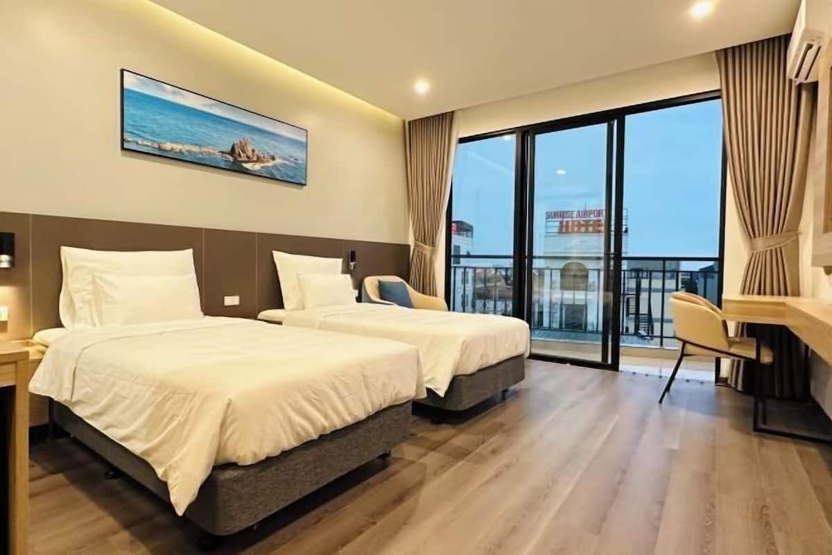 Ein Hotelzimmer mit zwei Betten, einem Schreibtisch, einem Stuhl, einem großen Fenster mit Blick auf den Flughafen und einem Gemälde an der Wand.