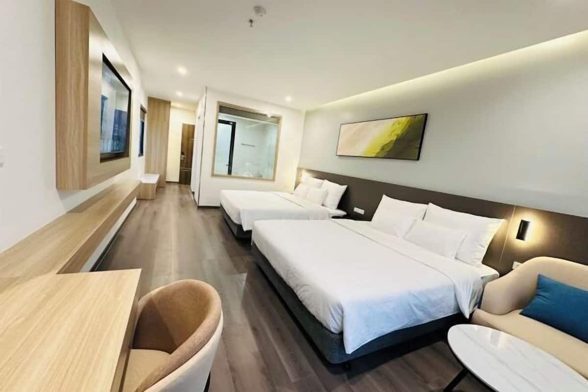 Ein Hotelzimmer mit zwei Betten, einer Couch, einem kleinen Tisch und einem an der Wand befestigten Fernseher.