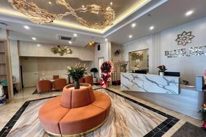 Een moderne hotellobby met een receptiebalie, een unieke zithoek in oranje en decoratieve muurkunst.