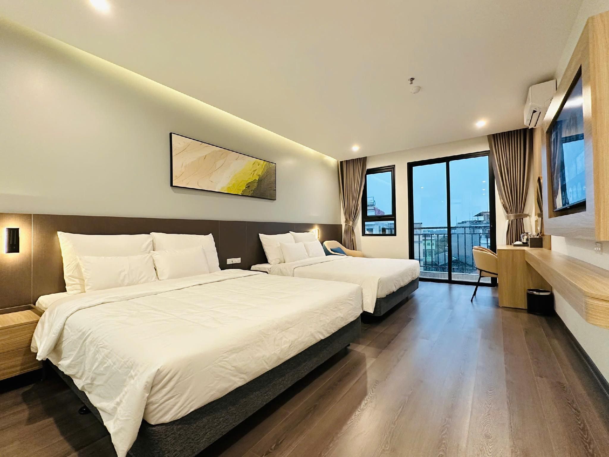 A hotel room with two beds, a large window with curtains, a mounted artwork, and a small desk area.