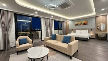 A modern hotel room with a sofa, a bed, a desk, and a view of the city at night.