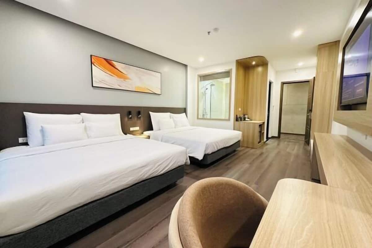 Ein Hotelzimmer mit zwei Betten, einem Schreibtisch, einem Stuhl, einem Fernseher und einem durch ein Fenster einsehbaren Badezimmer.