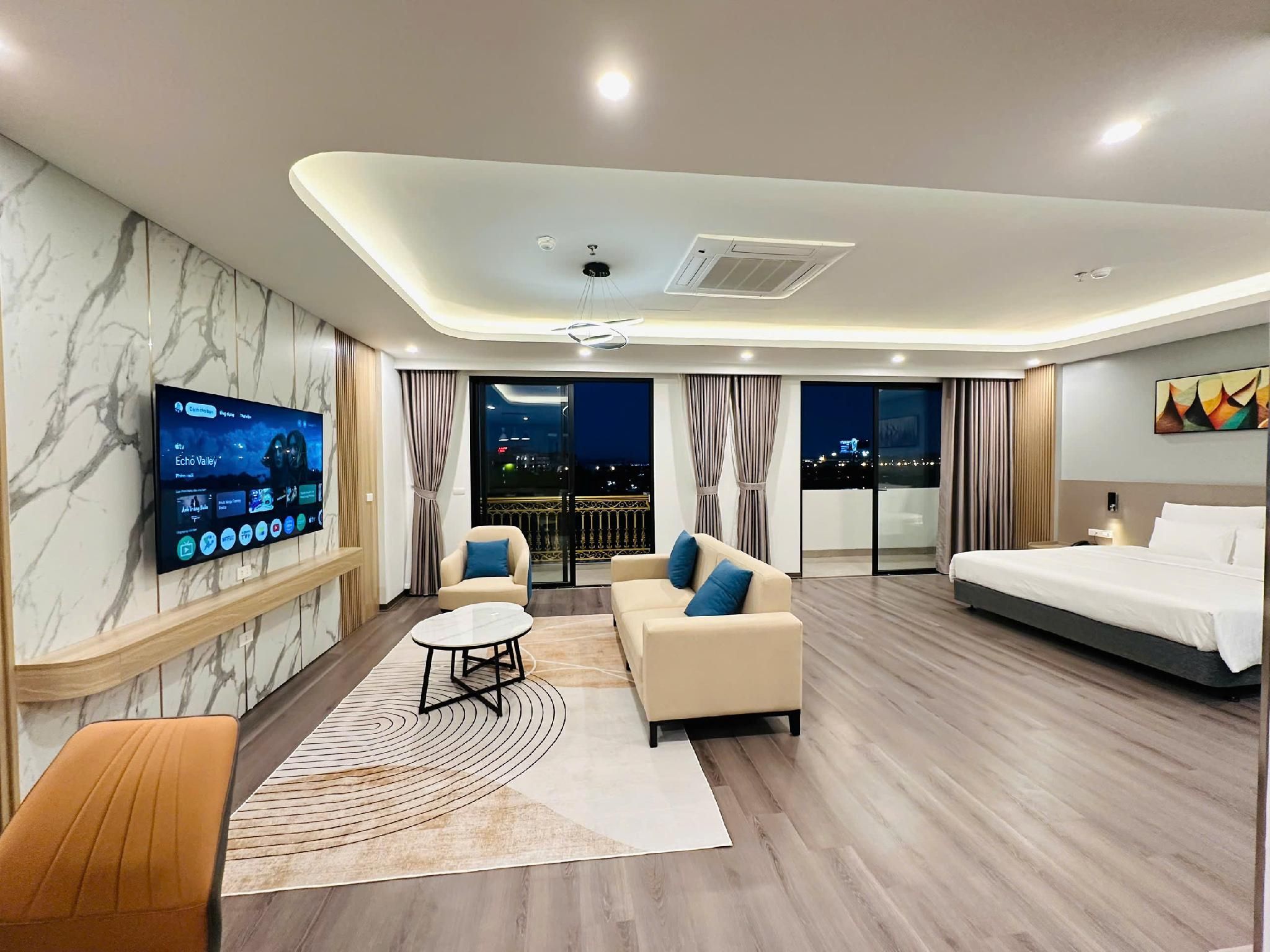 A modern hotel room with a TV, sofa, bed, and a view of the city at night.