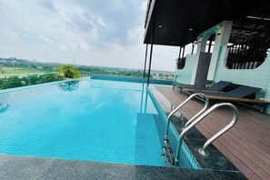 Une magnifique piscine à débordement d’un bleu profond, dotée d’une terrasse en bois et de chaises longues, offrant une vue imprenable sur un paysage pittoresque.