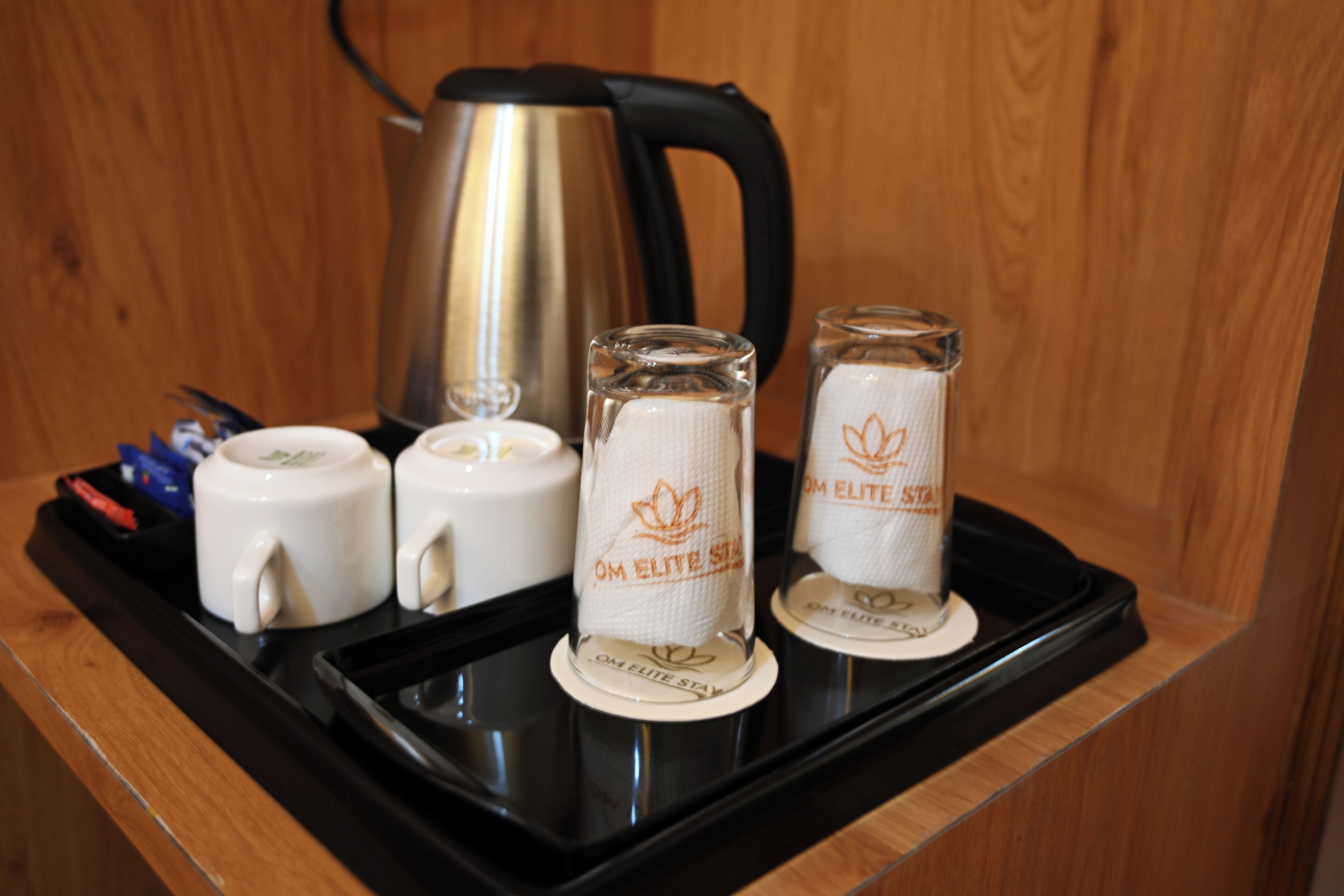 A tray with a kettle, two white mugs, and two glass tumblers with "OM ELITE STAR" branding.