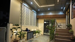 A hotel lobby with a reception desk, potted plants, a staircase, and a decorative wall.