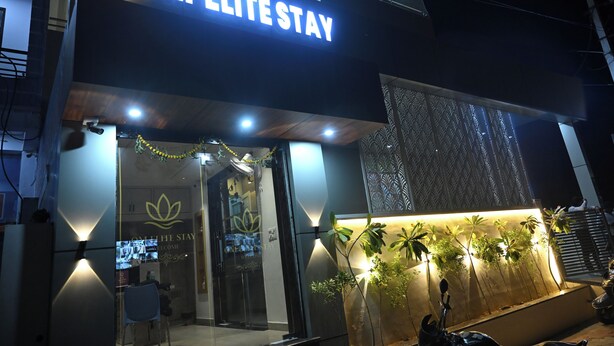 The exterior of OM ELITE STAY hotel with a prominent illuminated sign, a glass entrance, and a decorative plant wall.
