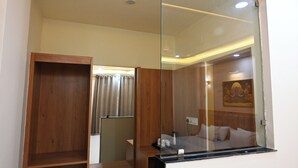 A hotel room with a wooden wardrobe, a bed with pillows, a nightstand, and a wall-mounted painting.