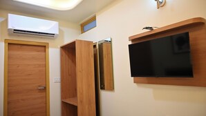 A room with a wooden door, an air conditioning unit, a television mounted on the wall, and a shelf.