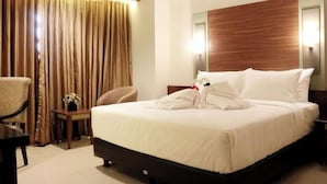 A hotel room with a bed, a chair, a nightstand, and a curtain. - Lume’os Hotel (Central Jakarta)