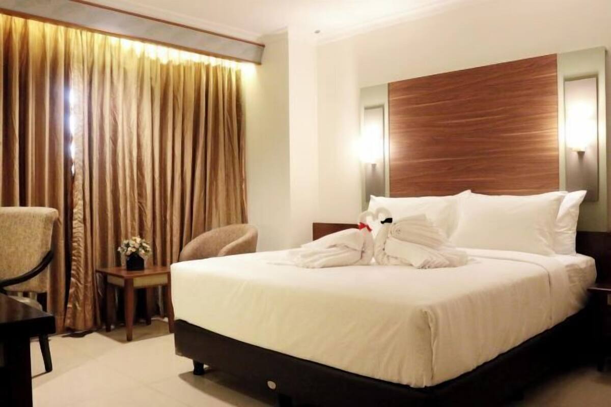 A hotel room with a bed, a chair, a nightstand, and a curtain.