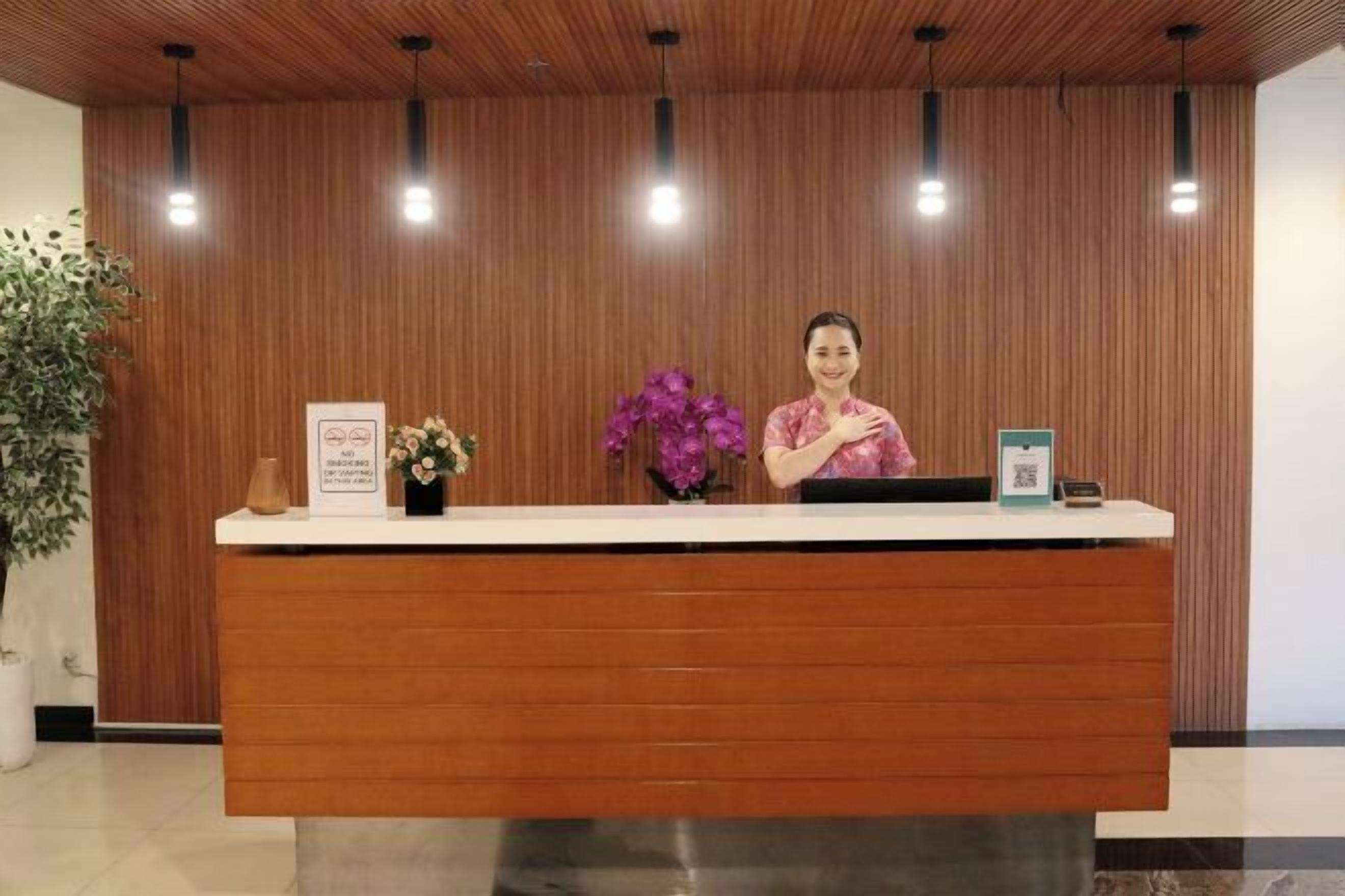 A reception desk with a wooden backdrop, a potted plant, and a sign indicating a smoking area.
