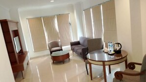 A spacious living area with a sofa, armchairs, a coffee table, and a TV stand. - Lume’os Hotel (Central Jakarta)