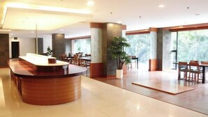 A spacious lobby with a wooden reception desk, large windows, and a potted plant. - Lume’os Hotel (Central Jakarta)