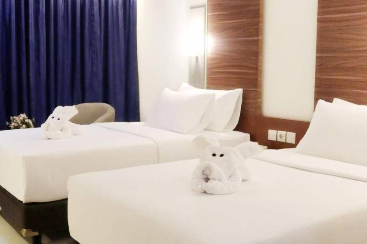 A hotel room with two beds, a chair, and a teddy bear on one bed.