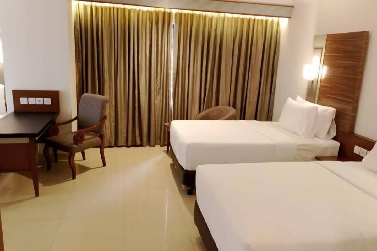 A hotel room with two beds, a desk, a chair, and a curtain.