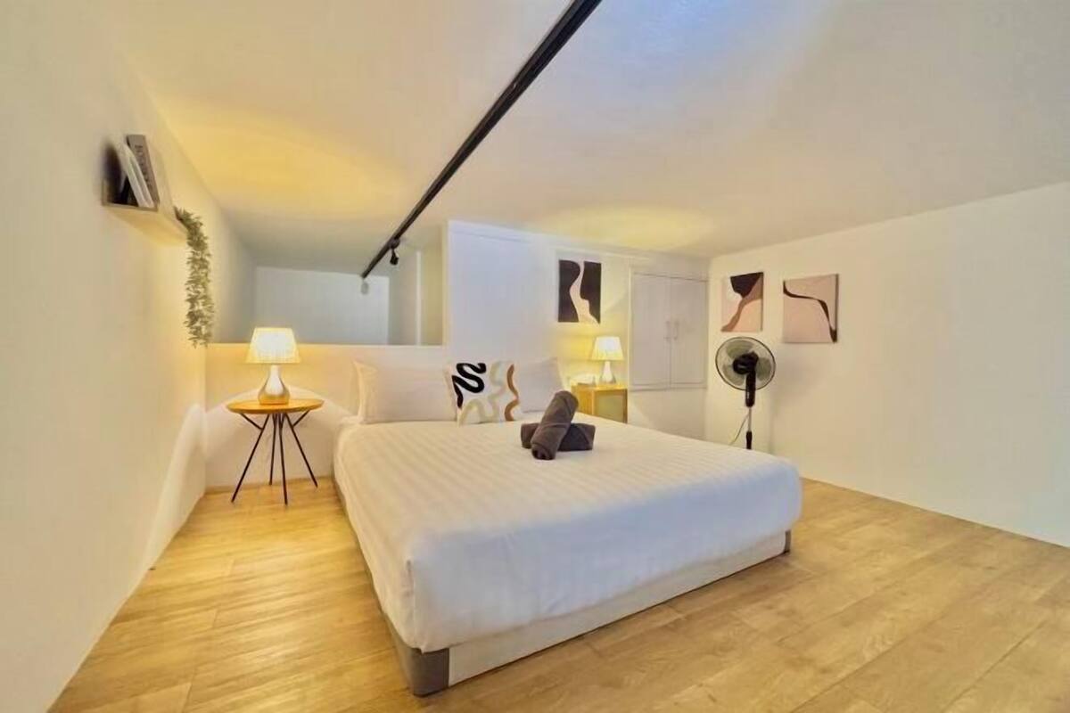 Un dormitorio con cama, lámparas de noche, una mesita y cuadros en la pared.