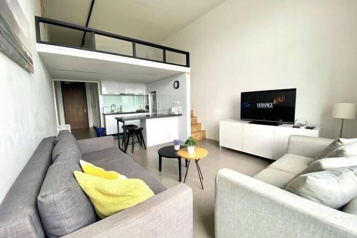 Una sala de estar moderna con un sofá, una mesa de centro, un televisor y una zona de cocina al fondo.