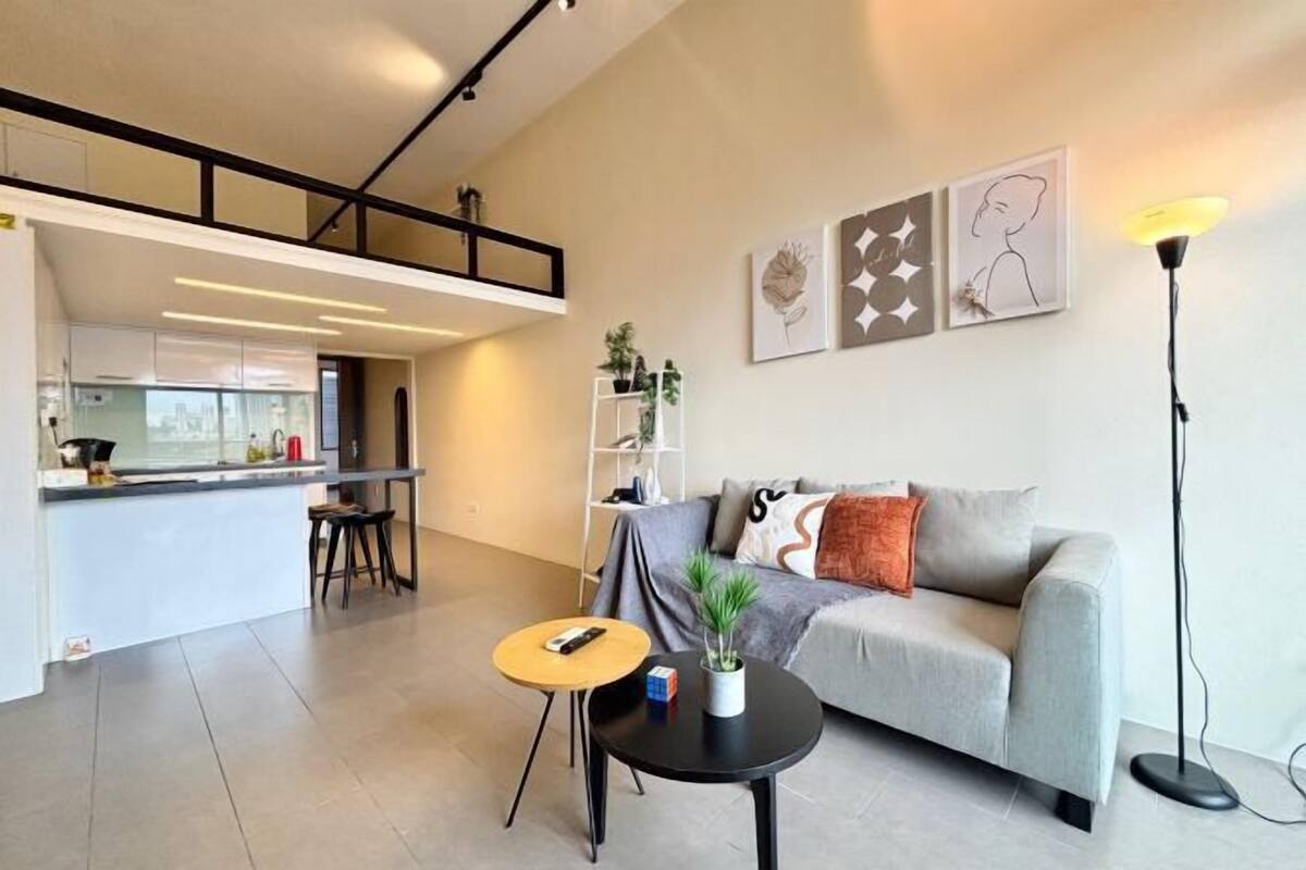 Un espacio habitable moderno con un sofá, una mesa de centro, una lámpara de pie y una cocina al fondo.