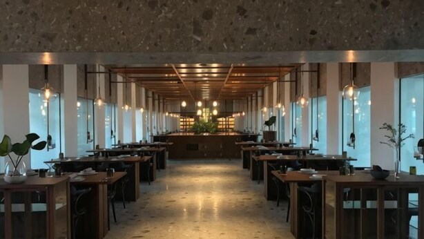 Un restaurant spacieux avec de longues tables, des luminaires suspendus et une allée centrale.