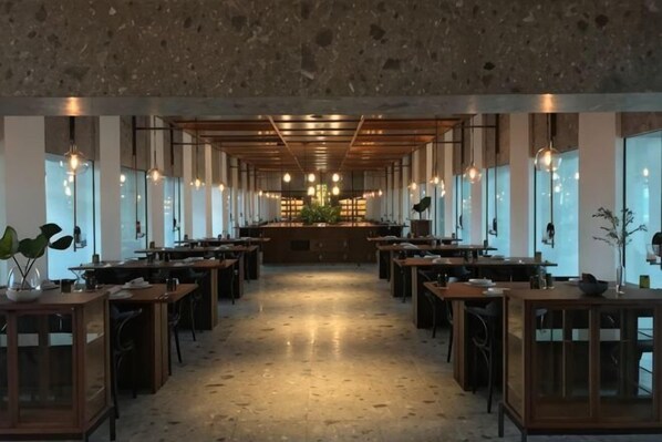 A spacious restaurant with long tables, pendant lighting, and a central walkway.