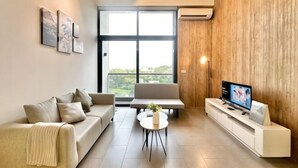 Un salon moderne avec un canapé, une table basse, un téléviseur posé sur un meuble blanc et une grande fenêtre donnant sur un beau paysage.
