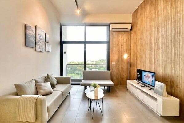 A modern living room with a sofa, a coffee table, a TV on a white stand, and a large window with a view. - The Establishment Bangsar by Lynhomes (Kuala Lumpur)
