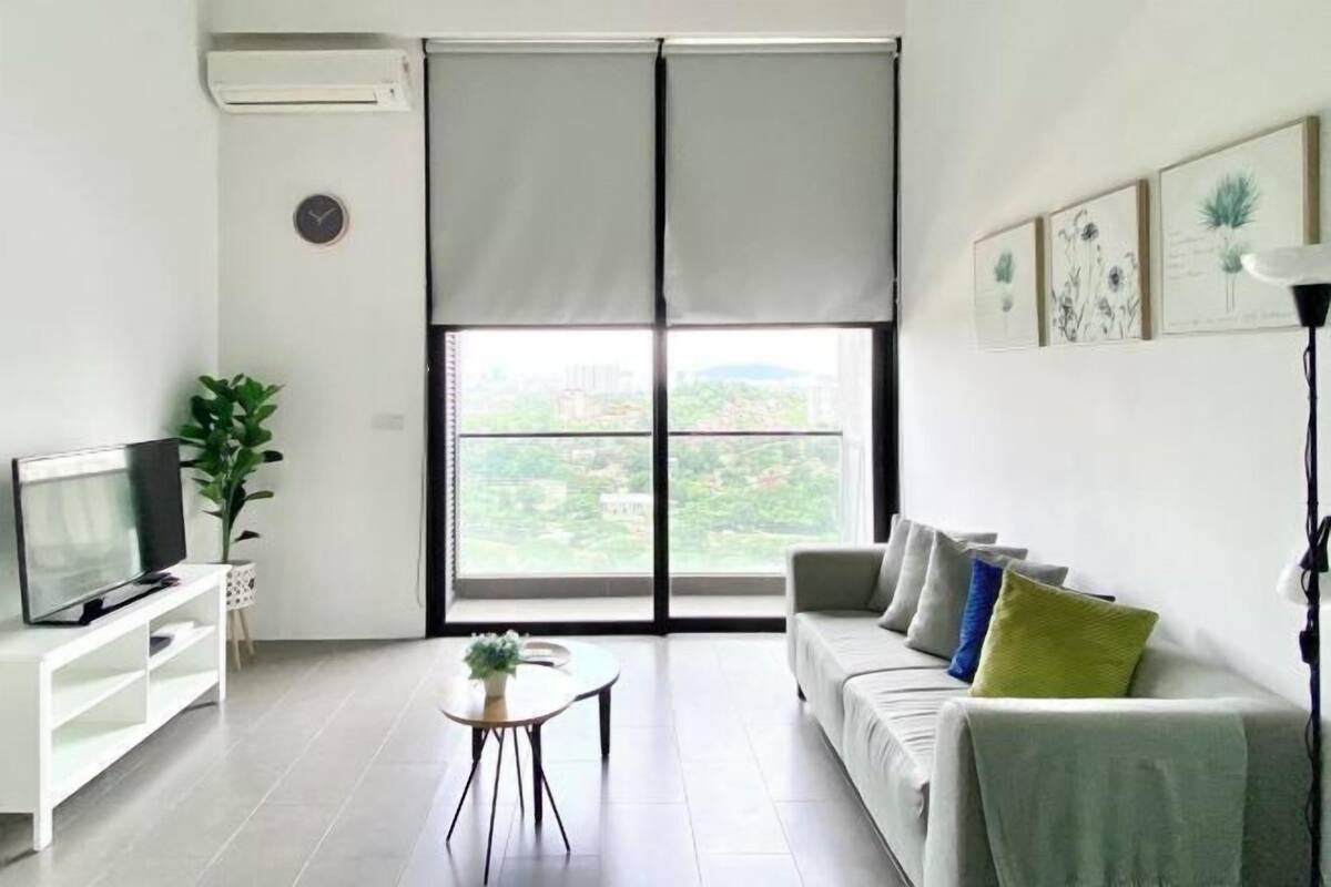 Un salón moderno con televisor, sofá y vistas a través de amplios ventanales.