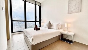 Une chambre d’hôtel moderne dotée d’une grande fenêtre, d’un lit, d’une table de chevet avec une lampe et d’un élément décoratif mural.