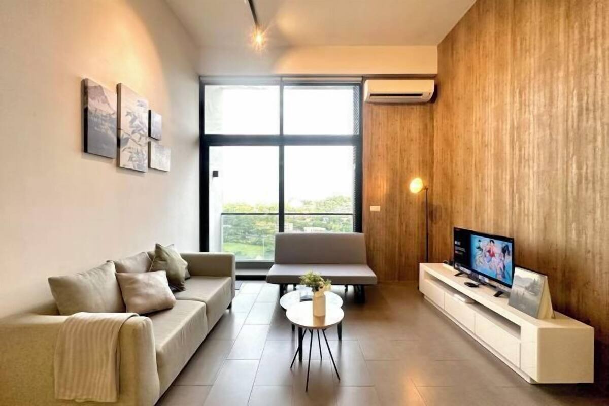Una sala de estar moderna con un sofá, una mesa de centro, un televisor sobre un mueble blanco y un amplio ventanal con vistas.