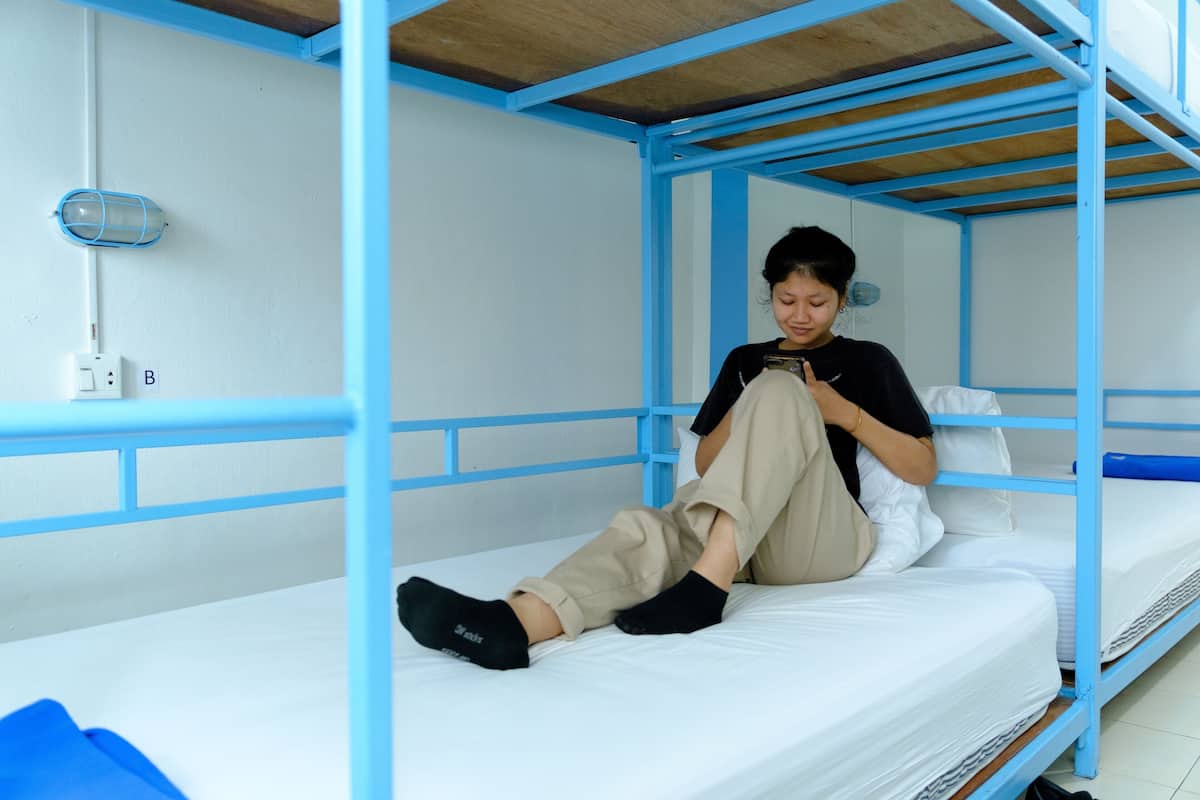 A bunk bed with a person sitting on the lower bunk, a blue metal frame, and a white mattress.