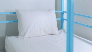 Un lit superposé avec un matelas et un oreiller blancs, une structure en métal bleue et un mur blanc.