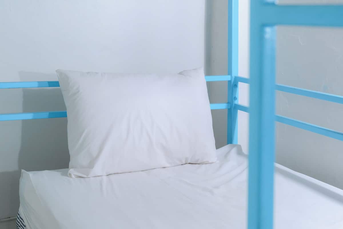 A bunk bed with a white mattress and pillow, blue metal frame, and a white wall.