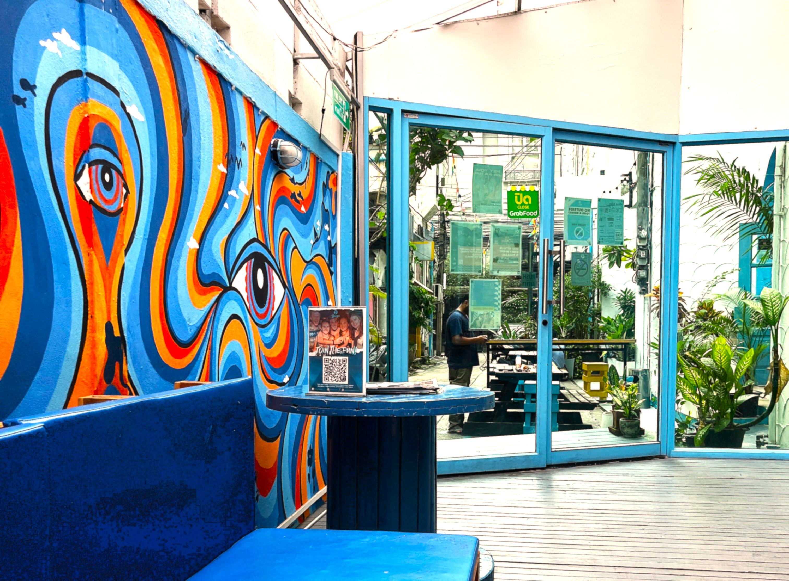 A colorful mural with an eye design, a blue bench, and a glass door entrance to a restaurant.