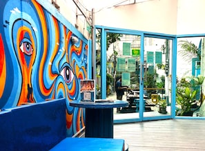 A colorful mural with an eye design, a blue bench, and a glass door entrance to a restaurant. - Bodega Soi 23 Bangkok (Bangkok)