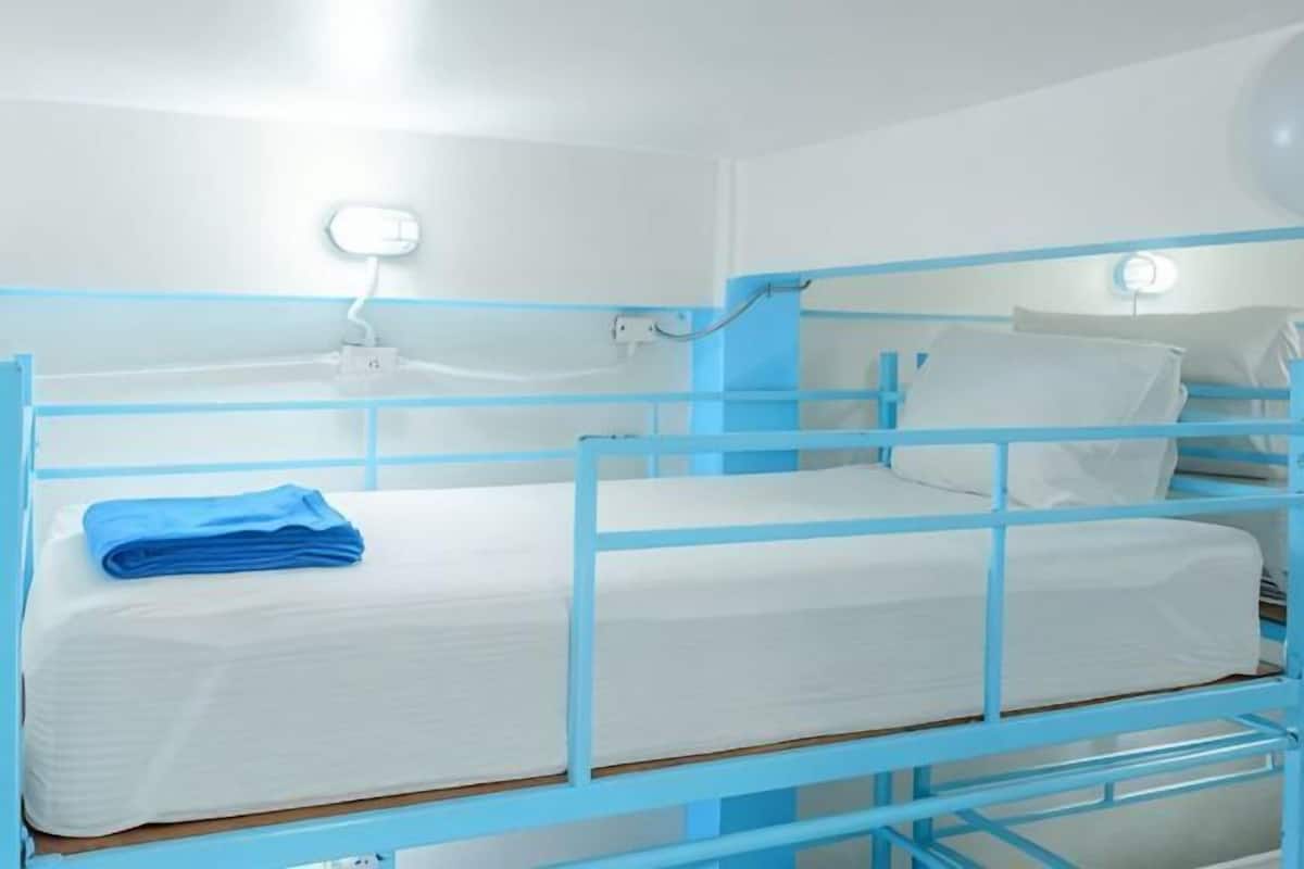 A bunk bed room with a blue frame, white bedding, and a wall socket.