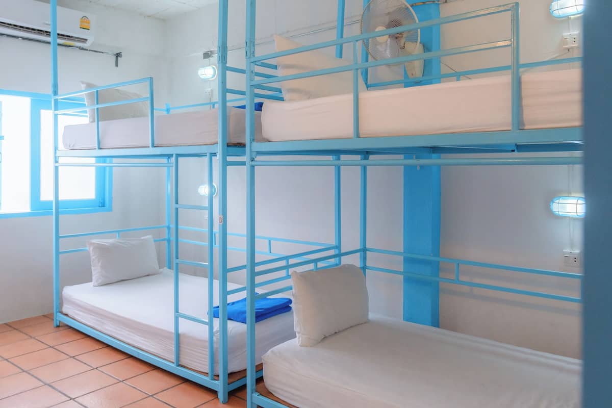 A bunk bed room with blue railings, white bedding, and a window with blinds.