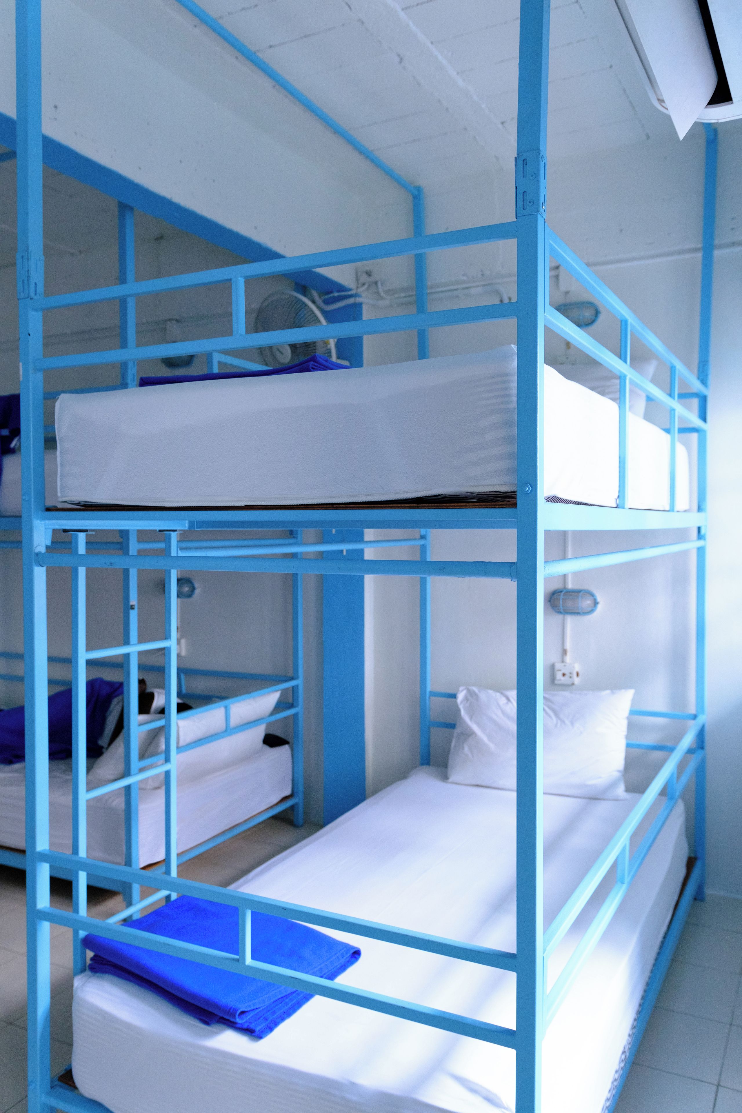 Habitació amb lliteres de blau metàl·lic, roba de llit blanca i una tovallola blava petita al llit inferior.