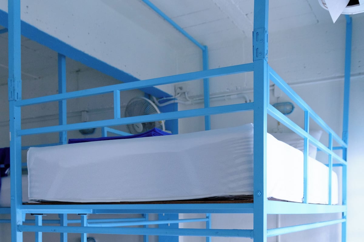 A bunk bed room with a blue metal frame, white bedding, and a small blue towel on the lower bunk.