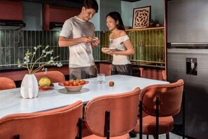 A dining area with a table set for two, a vase with flowers, and a bowl of fruit. - Express by M Village Vo Van Kiet, a brand of Modern Village Lifestyle (Ho Chi Minh City)