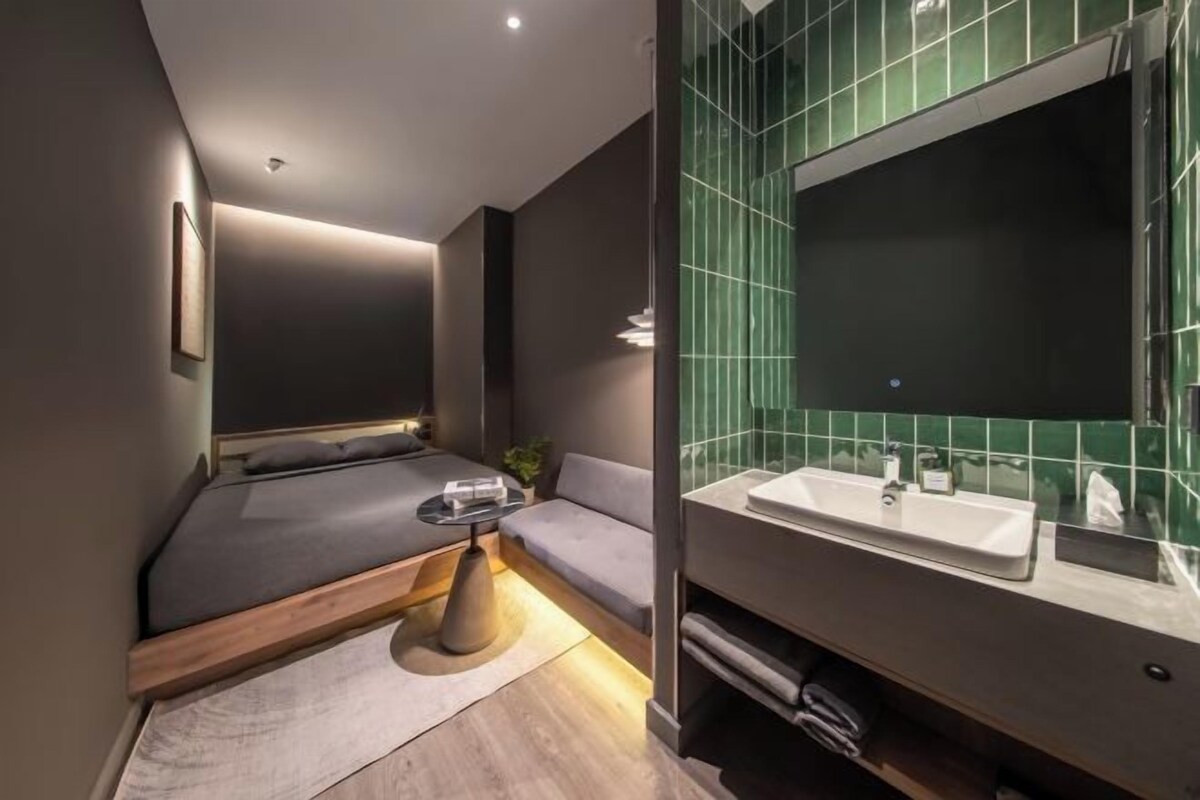 Ein modernes Schlafzimmer mit einem Bett, einem Nachttisch und einem großen Spiegel über einem Waschbecken.
