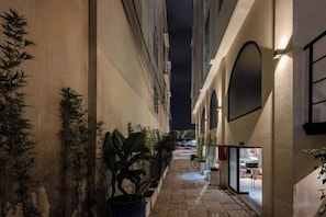 A narrow corridor with potted plants, a tiled floor, and a building entrance with a glass door. - Express by M Village Vo Van Kiet, a brand of Modern Village Lifestyle (Ho Chi Minh City)