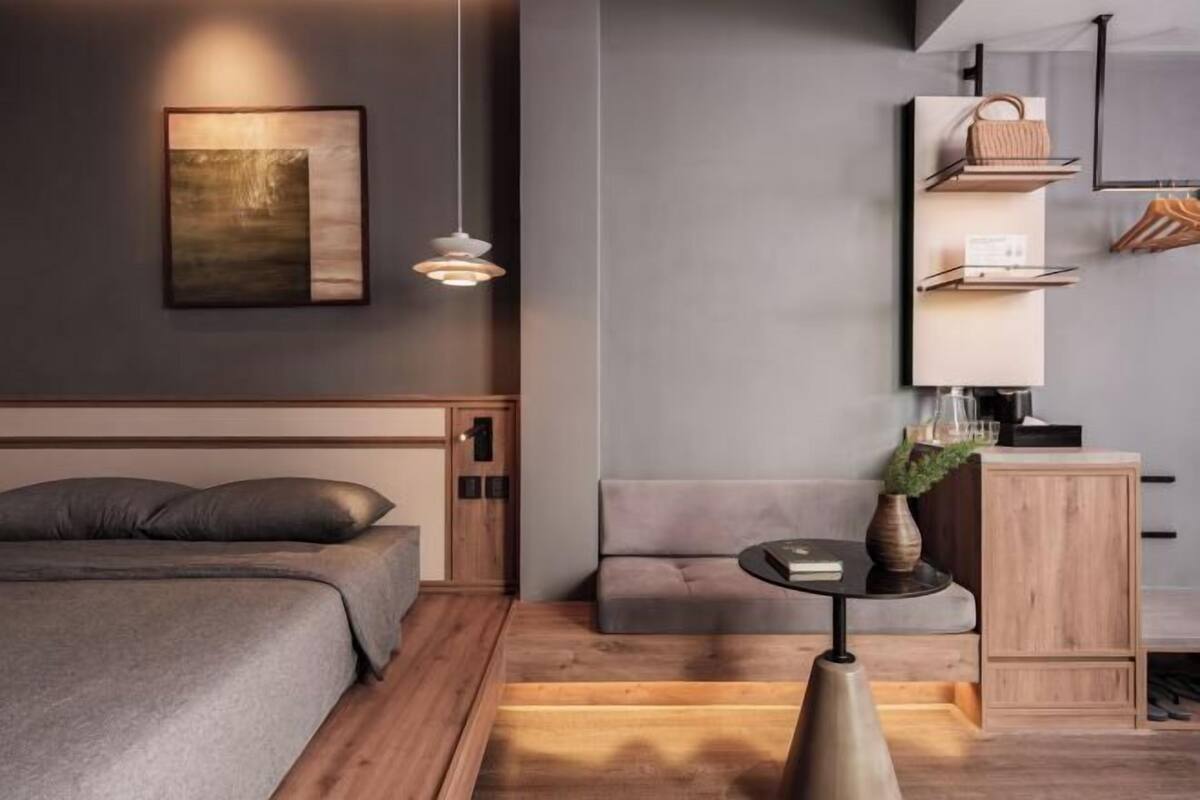 A modern bedroom with a bed, a bedside table, a wall-mounted shelf with a handbag, and a painting.
