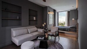 A modern living room with a sofa, a round coffee table, and a chair. There are shelves on the wall and a window with a view. - Express by M Village Vo Van Kiet, a brand of Modern Village Lifestyle (Ho Chi Minh City)