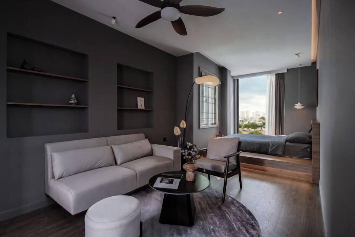 A modern living room with a sofa, a round coffee table, and a chair. There are shelves on the wall and a window with a view.