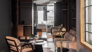 A modern living room with a sofa, a chair, a coffee table, and a vase with flowers. There is a bookshelf and a window with a view of the city. - Express by M Village Vo Van Kiet, a brand of Modern Village Lifestyle (Ho Chi Minh City)