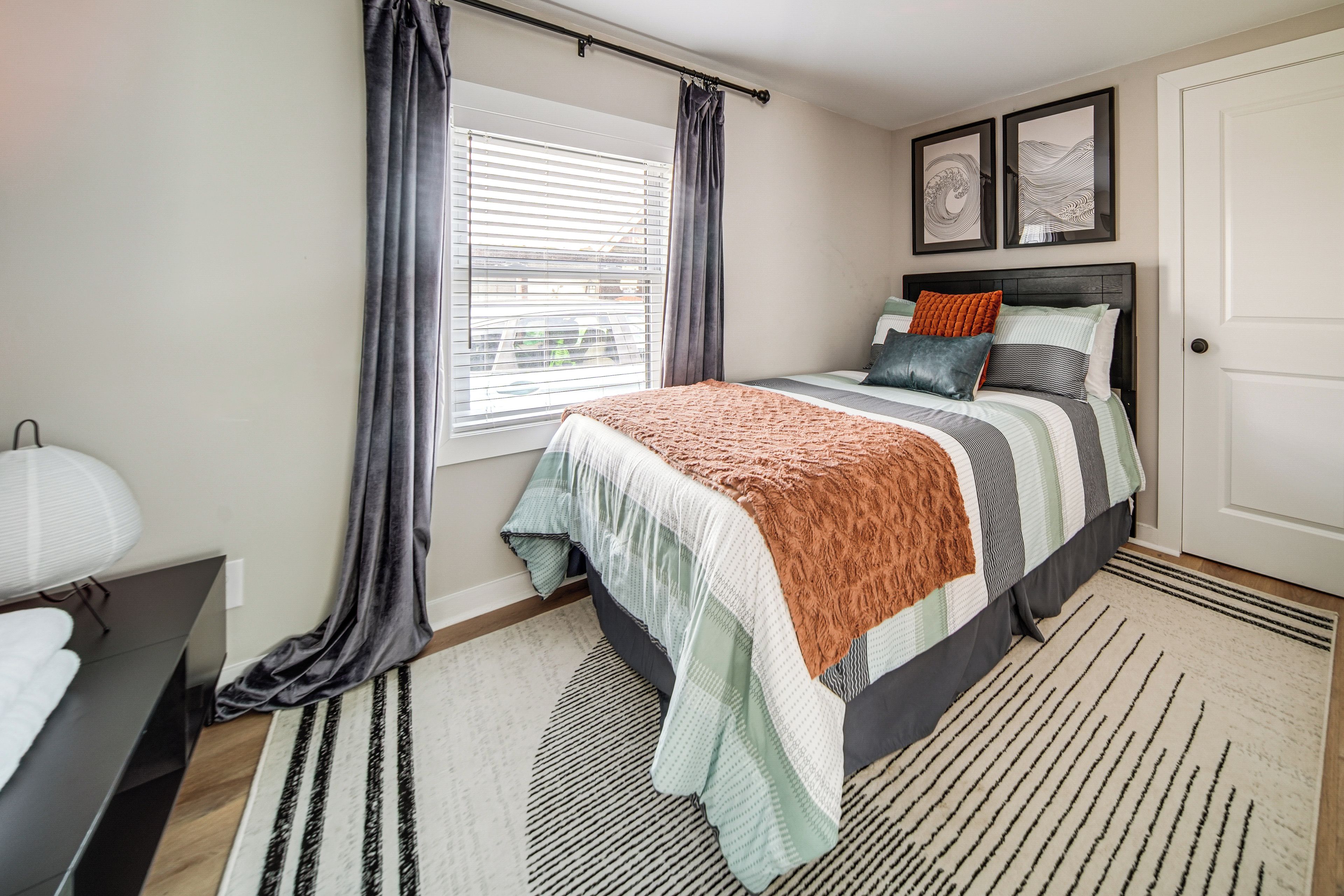 A bedroom with a bed, a window with curtains, a bedside table, and a door.